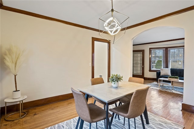 dining area featuring ornamental molding, arched walkways, baseboards, and wood finished floors