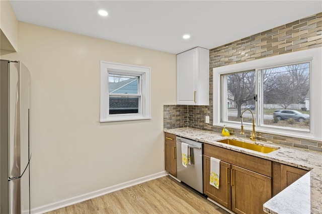 kitchen featuring light stone countertops, stainless steel appliances, tasteful backsplash, a sink, and light wood-style floors