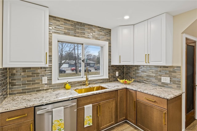 kitchen with stainless steel dishwasher, backsplash, a sink, and light stone counters