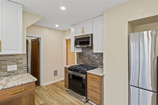 kitchen featuring light wood-type flooring, light stone counters, visible vents, white cabinets, and appliances with stainless steel finishes