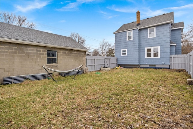 back of property featuring a chimney, a fenced backyard, roof with shingles, and a yard
