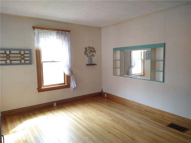 unfurnished room with baseboards, visible vents, wood finished floors, and ornamental molding