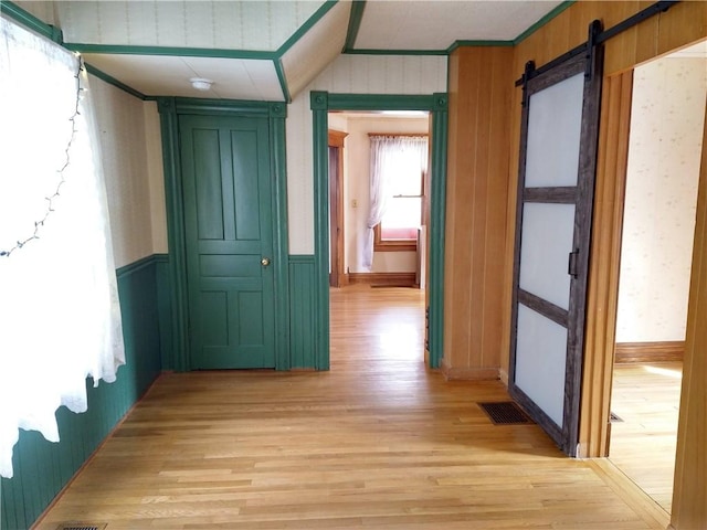 corridor with wallpapered walls, a barn door, light wood finished floors, and visible vents