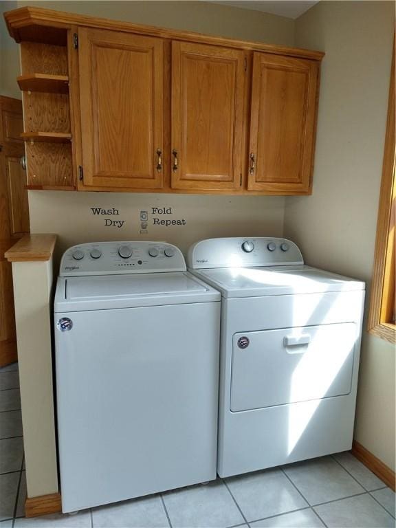 clothes washing area with independent washer and dryer, cabinet space, baseboards, and light tile patterned floors