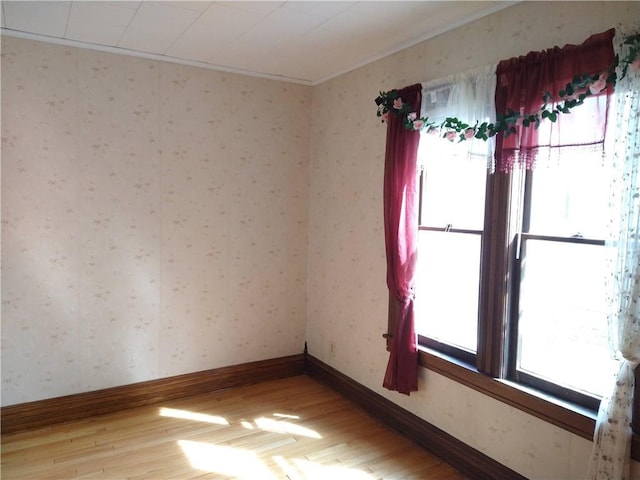 empty room with baseboards, wallpapered walls, and light wood-style flooring