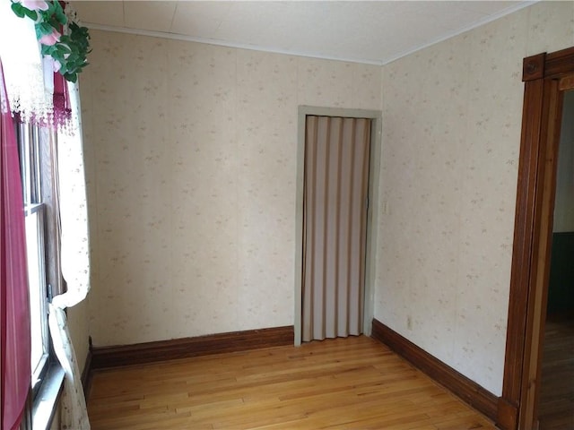 spare room featuring baseboards, wallpapered walls, and light wood finished floors