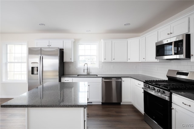 kitchen with dark stone countertops, a sink, decorative backsplash, white cabinetry, and appliances with stainless steel finishes