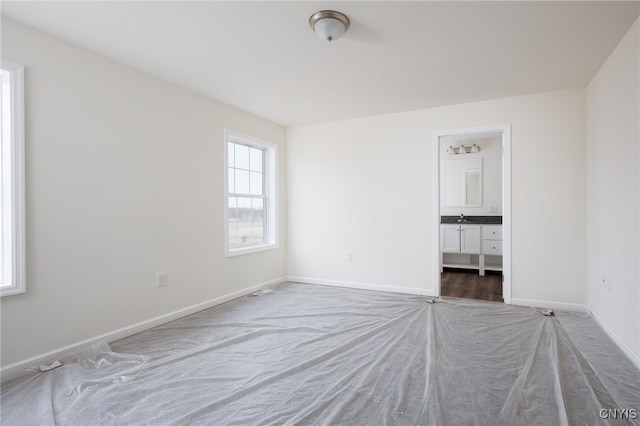 unfurnished bedroom with baseboards, ensuite bath, carpet flooring, and a sink