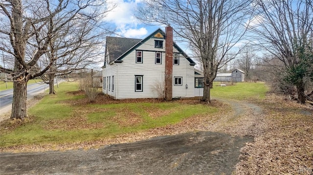view of side of property featuring a lawn, driveway, and a chimney