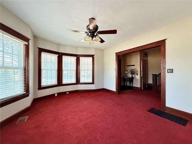 unfurnished room with a textured ceiling, ceiling fan, visible vents, and dark colored carpet