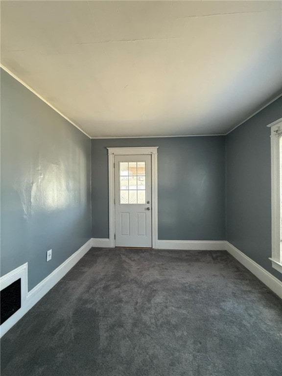 spare room featuring baseboards, visible vents, crown molding, and dark carpet