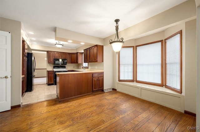 kitchen with light countertops, a sink, light wood finished floors, a peninsula, and black appliances