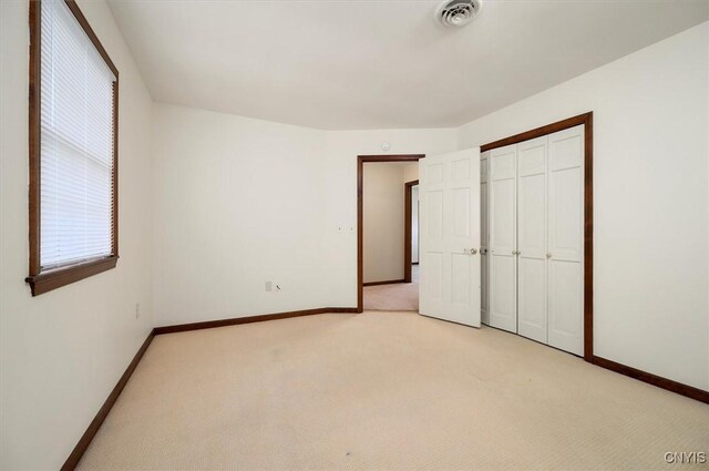 unfurnished bedroom with light carpet, baseboards, visible vents, and a closet