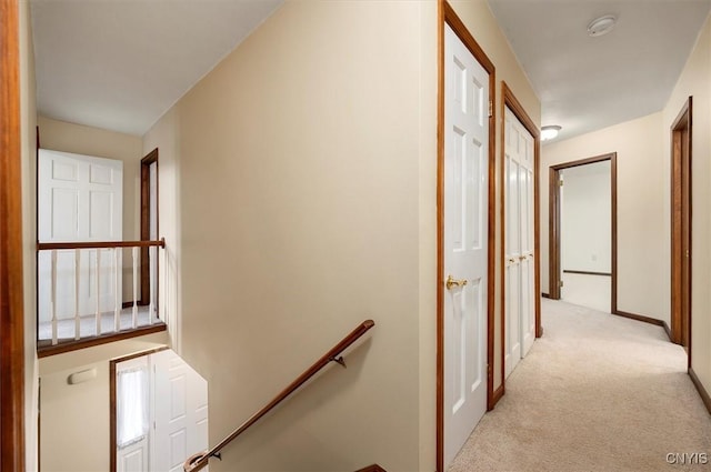 hallway featuring baseboards, an upstairs landing, and light colored carpet