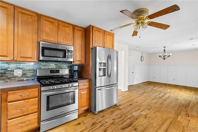 kitchen featuring ceiling fan with notable chandelier, dark countertops, light wood-type flooring, and appliances with stainless steel finishes