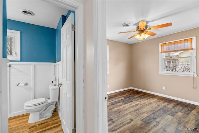 bathroom with visible vents, ceiling fan, toilet, wood finished floors, and wainscoting