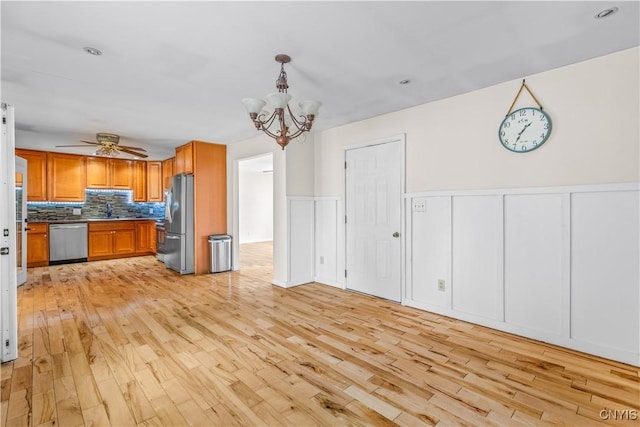 kitchen with ceiling fan with notable chandelier, backsplash, light wood finished floors, appliances with stainless steel finishes, and brown cabinetry