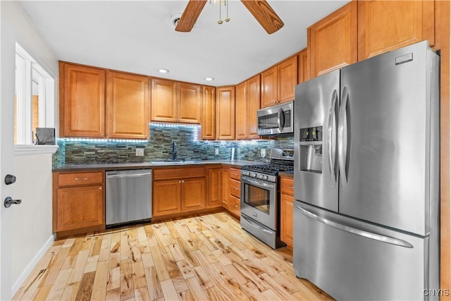 kitchen featuring backsplash, a sink, light wood-style floors, ceiling fan, and appliances with stainless steel finishes