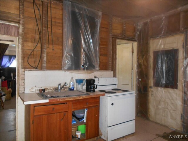 kitchen featuring light countertops, wooden walls, brown cabinets, a sink, and white range with electric stovetop