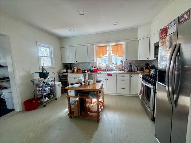 kitchen featuring crown molding, light wood-type flooring, decorative backsplash, white cabinets, and appliances with stainless steel finishes