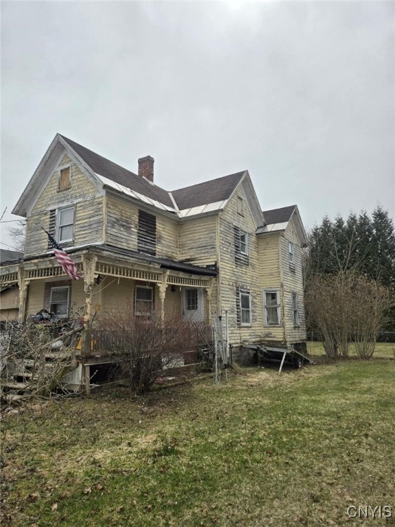 rear view of property featuring a chimney, covered porch, and a yard