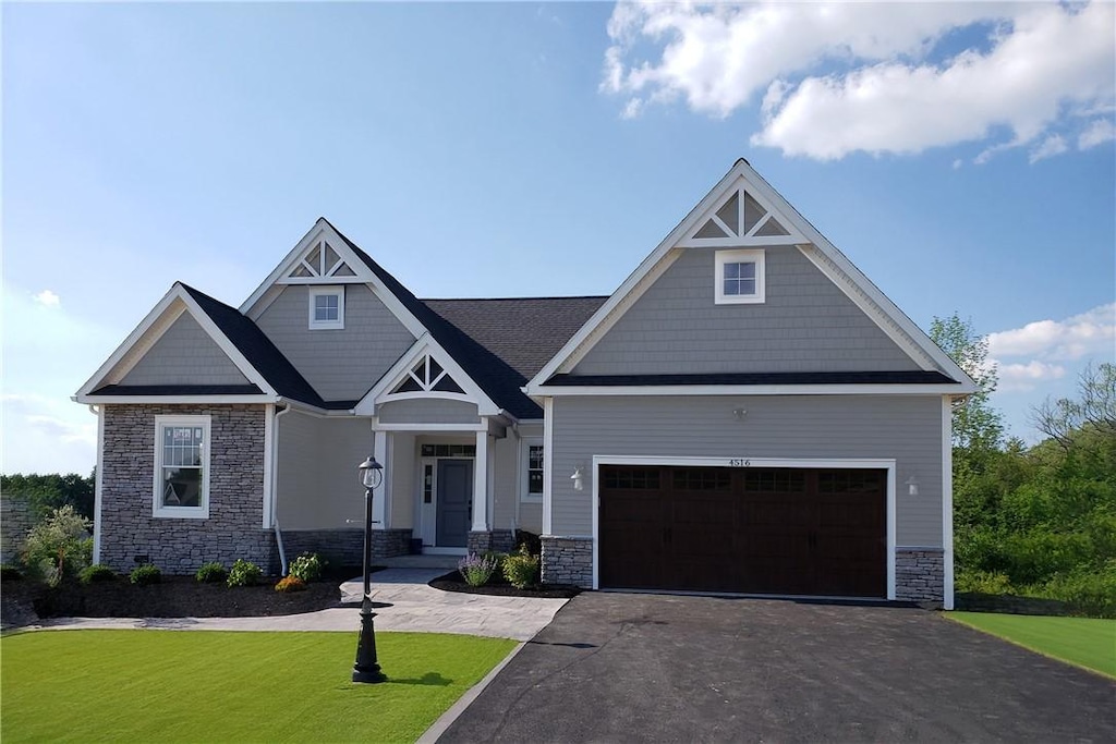 craftsman inspired home with stone siding, aphalt driveway, an attached garage, and a front yard