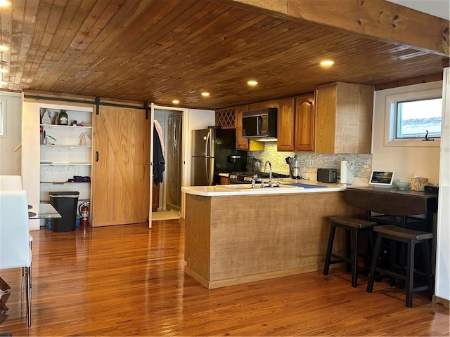 kitchen featuring black microwave, freestanding refrigerator, wooden ceiling, and a barn door
