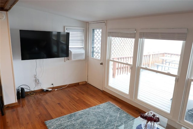 unfurnished living room with cooling unit, wood finished floors, baseboards, and lofted ceiling
