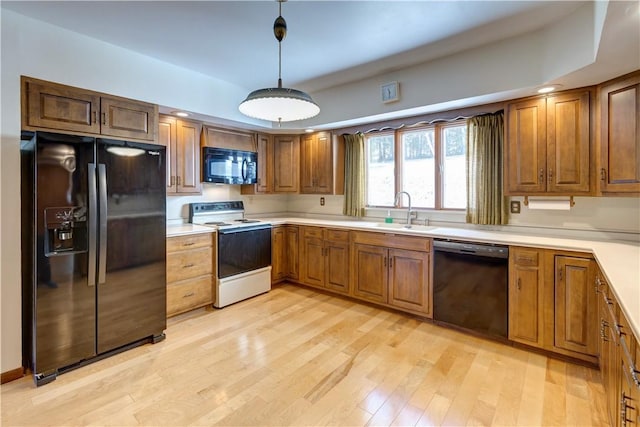 kitchen featuring light countertops, a sink, light wood-style floors, and black appliances