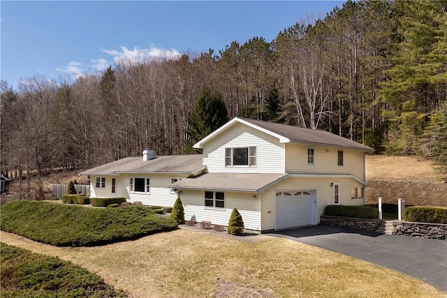 view of front of home featuring a front yard, a garage, a wooded view, and aphalt driveway