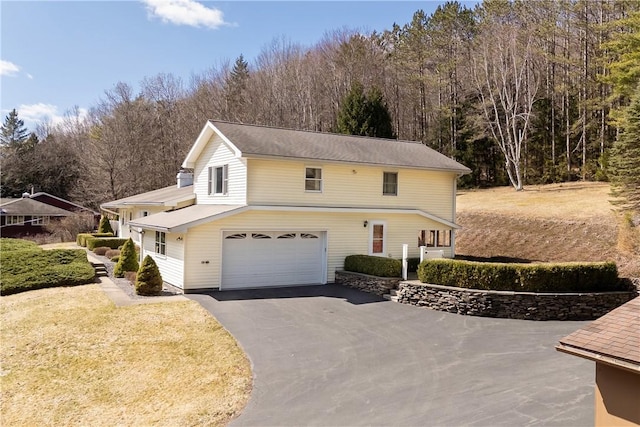 traditional-style house with a front lawn, driveway, a garage, and a forest view