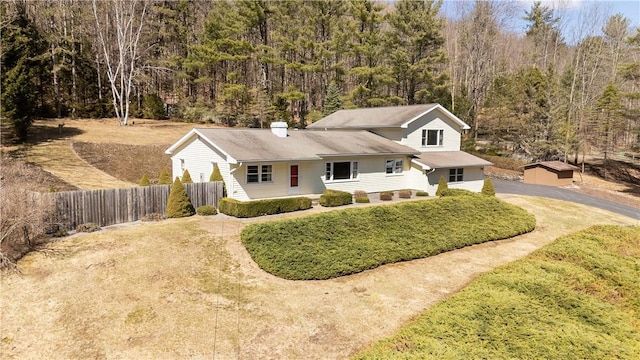 view of front of home with a chimney, fence, a forest view, and driveway