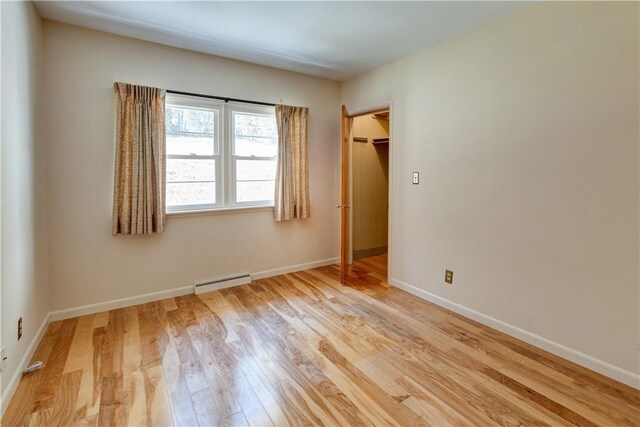 unfurnished bedroom featuring baseboards, a baseboard heating unit, and light wood-type flooring