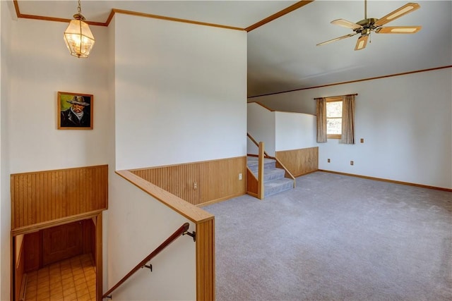 carpeted empty room with ornamental molding, wood walls, ceiling fan, and stairway