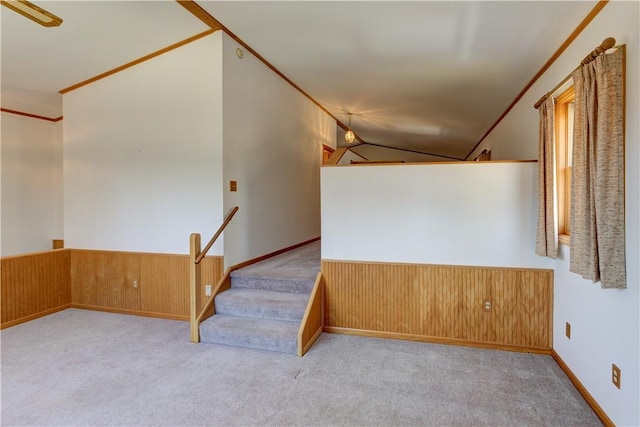 interior space with carpet flooring, a wainscoted wall, ornamental molding, and vaulted ceiling
