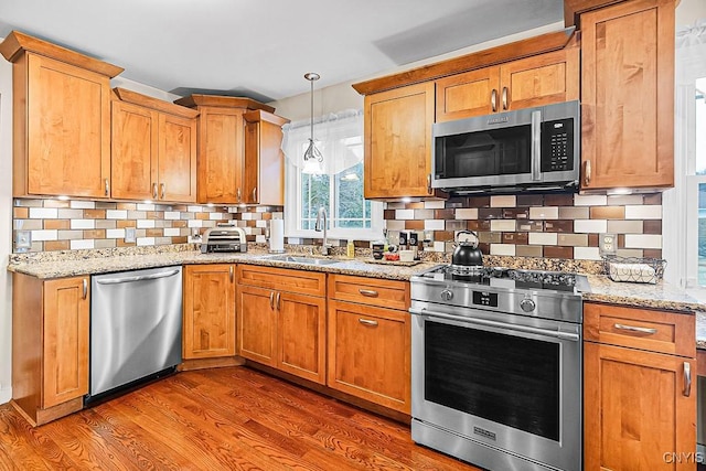 kitchen with tasteful backsplash, dark wood-style flooring, stainless steel appliances, a sink, and light stone counters