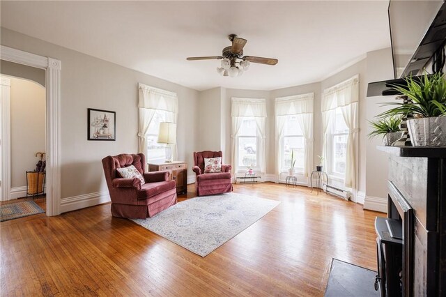 living area featuring baseboards, baseboard heating, wood finished floors, and a ceiling fan