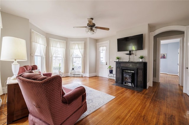 living area featuring baseboards, wood finished floors, a wood stove, and a ceiling fan