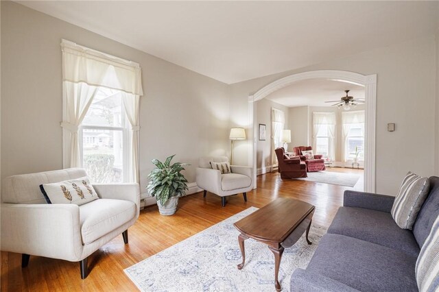 living room with arched walkways, baseboards, wood finished floors, and a ceiling fan