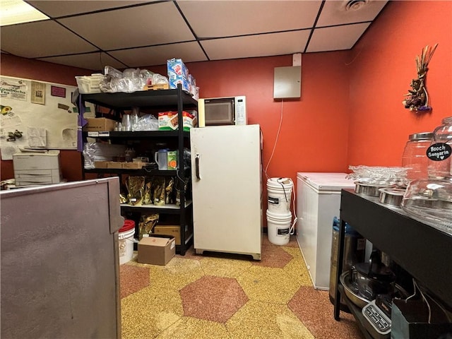 interior space featuring freestanding refrigerator, tile patterned floors, and a drop ceiling