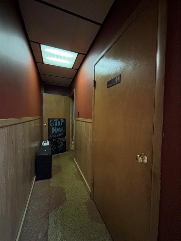 hall featuring a wainscoted wall, wooden walls, and a paneled ceiling