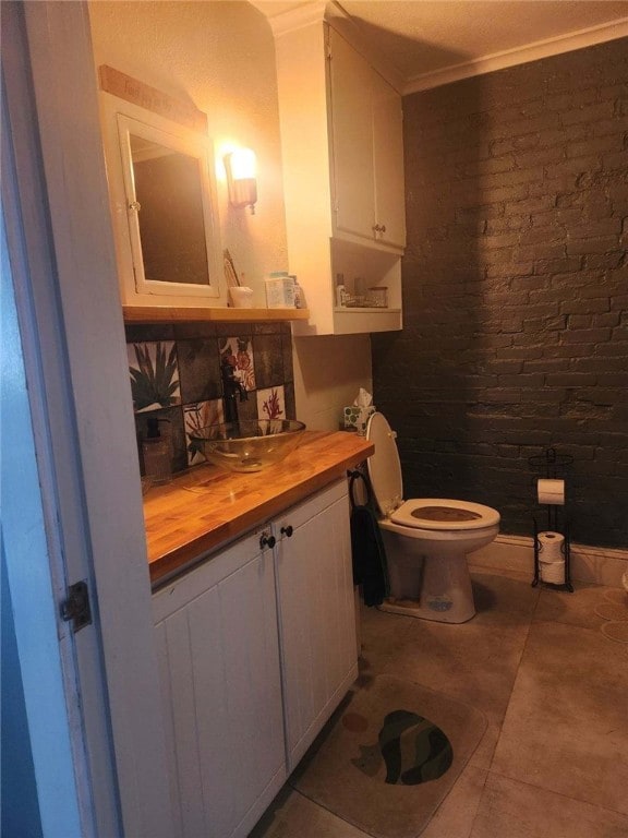 half bathroom with tile patterned floors, crown molding, toilet, and brick wall