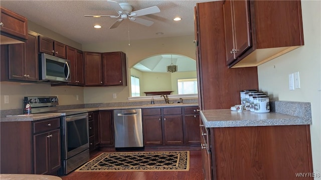 kitchen featuring a textured ceiling, a sink, arched walkways, a ceiling fan, and appliances with stainless steel finishes