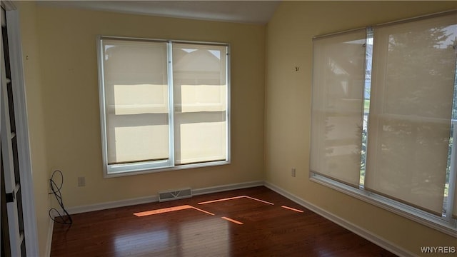 spare room with wood finished floors, plenty of natural light, baseboards, and visible vents