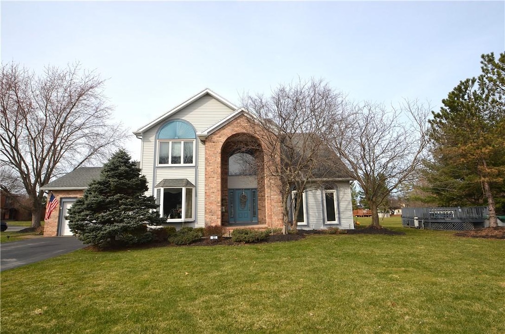 traditional-style home with driveway, a garage, brick siding, and a front yard