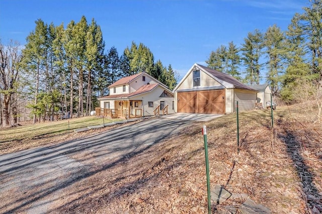 view of front of house featuring covered porch, gravel driveway, an outbuilding, and a garage