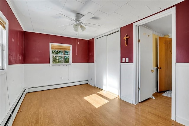 spare room featuring light wood finished floors, ceiling fan, and baseboard heating