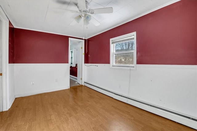 spare room featuring ceiling fan, wood finished floors, a baseboard heating unit, and wainscoting