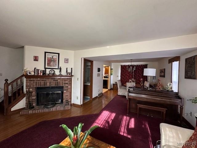 living area featuring baseboards, a notable chandelier, wood finished floors, and a brick fireplace