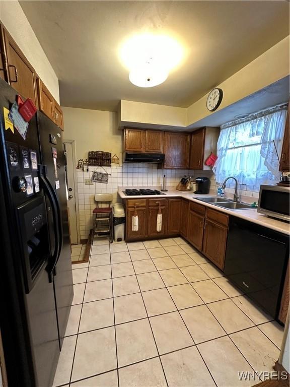 kitchen with black appliances, under cabinet range hood, a sink, and light countertops
